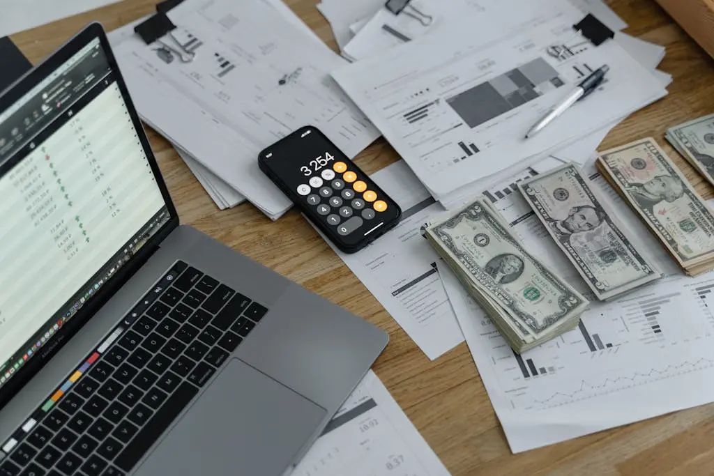 A desk with cash or accrual nonprofit financial documents, currency, a laptop, and phone calculator.