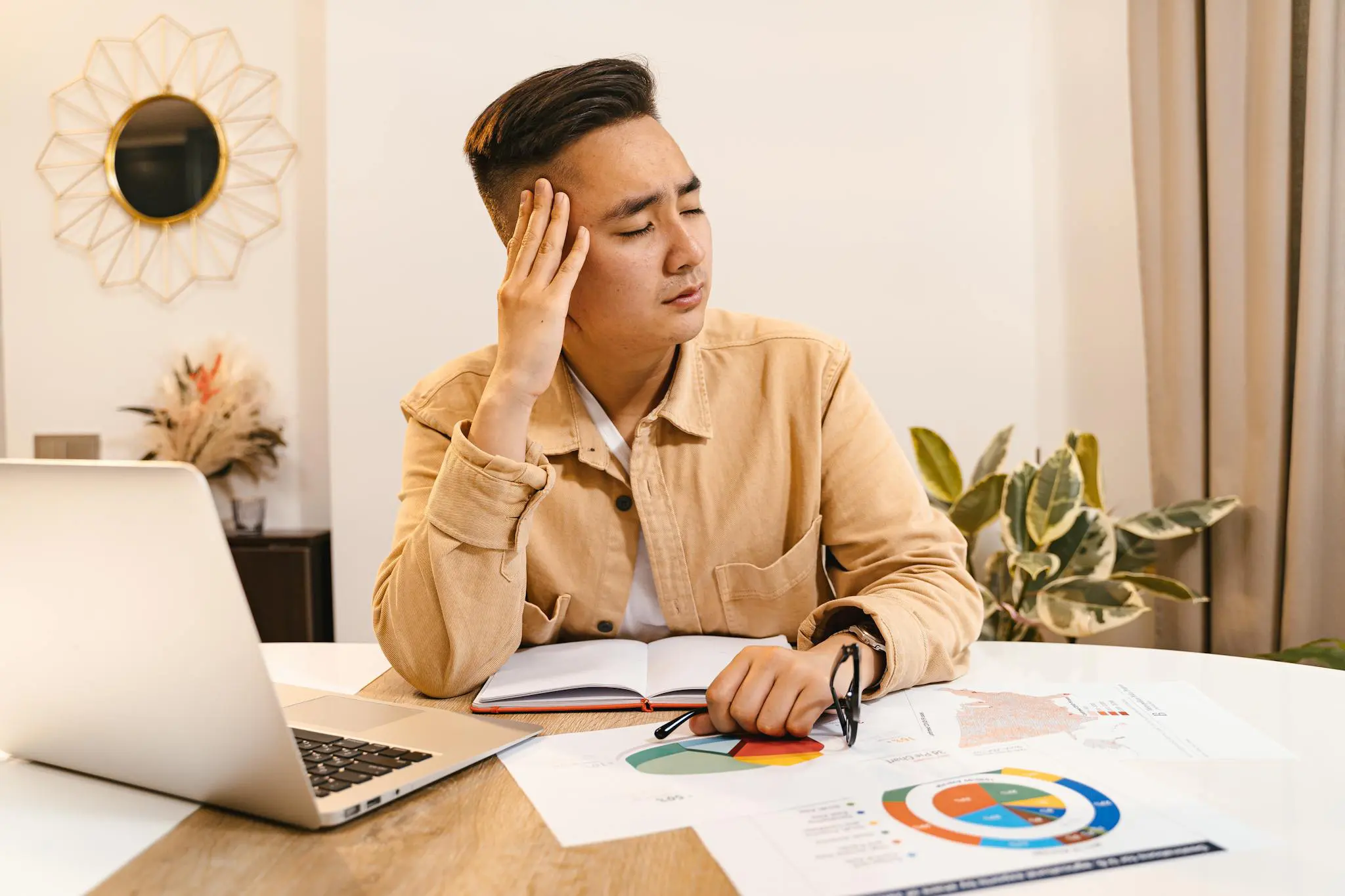 Nonprofit professional holding head in frustration, surrounded by financial documents and laptop at office.
