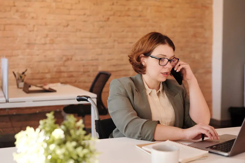 Professional female virtual bookkeeper in wheelchair working remotely on laptop and phone in a modern office.
