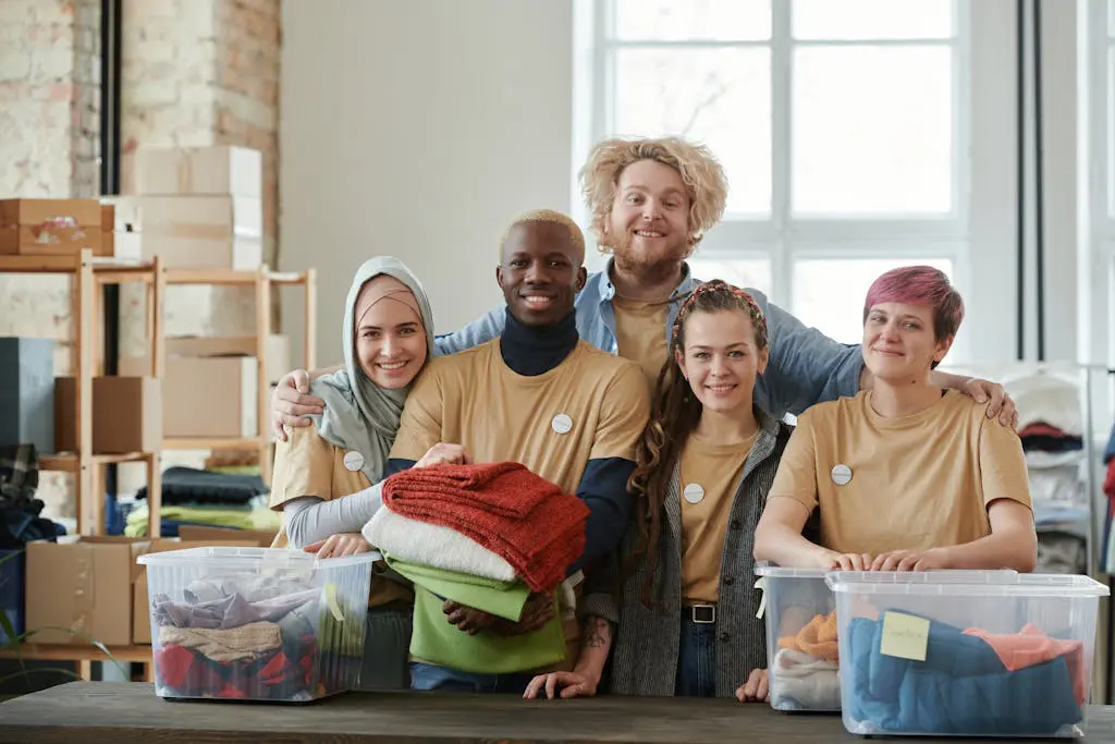 Group of diverse volunteers smiling while sorting clothes at a charity donation center.
