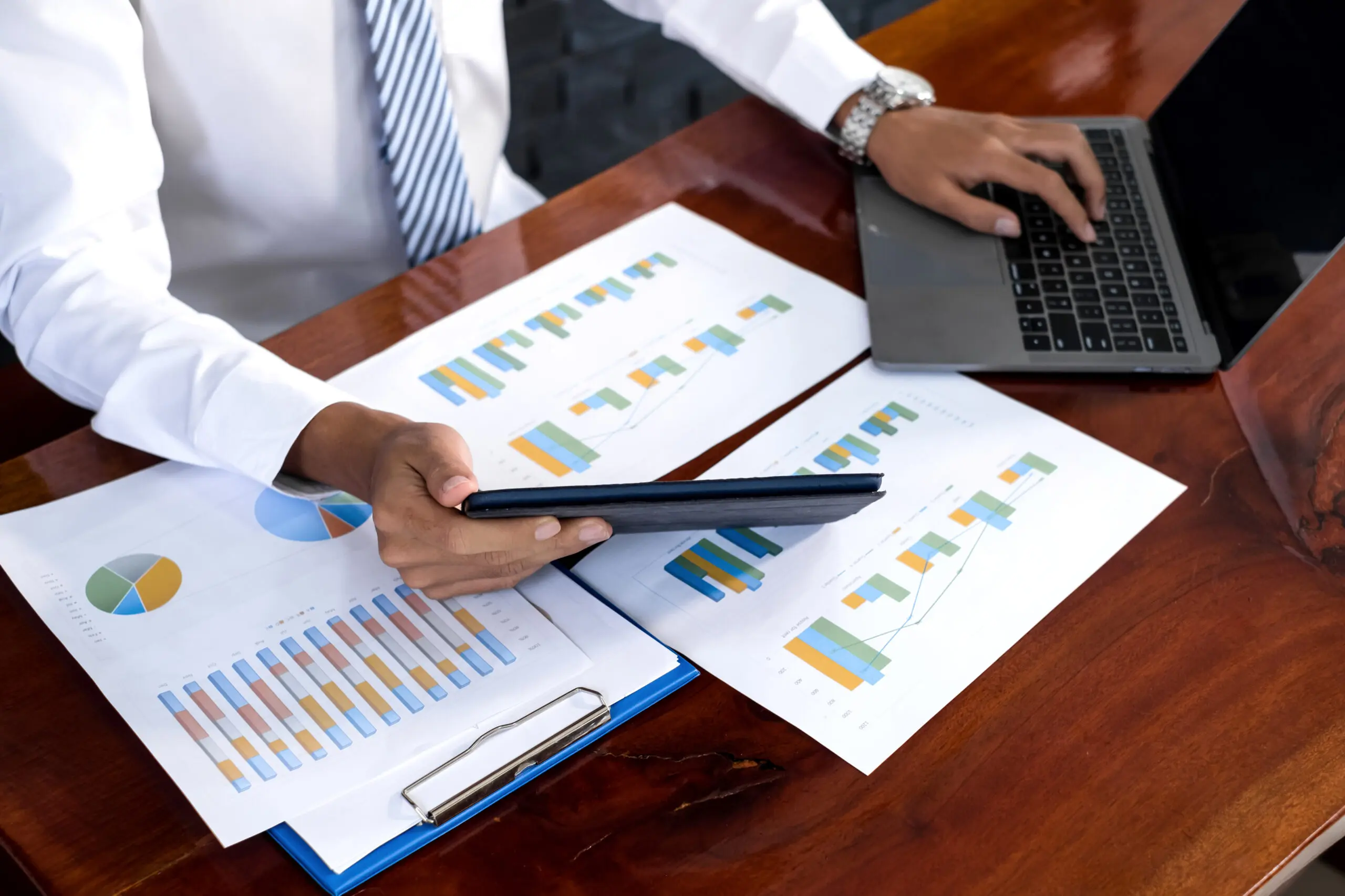 Person sitting at a desk comparing paper reports of various income streams.