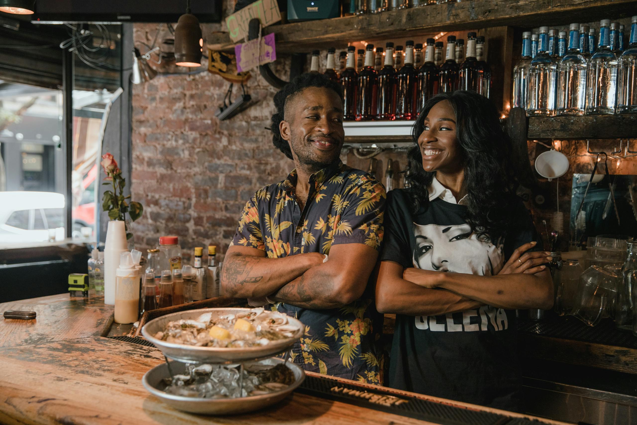 Two business owners smiling confidently behind a bar after outsourcing their bookkeeping.