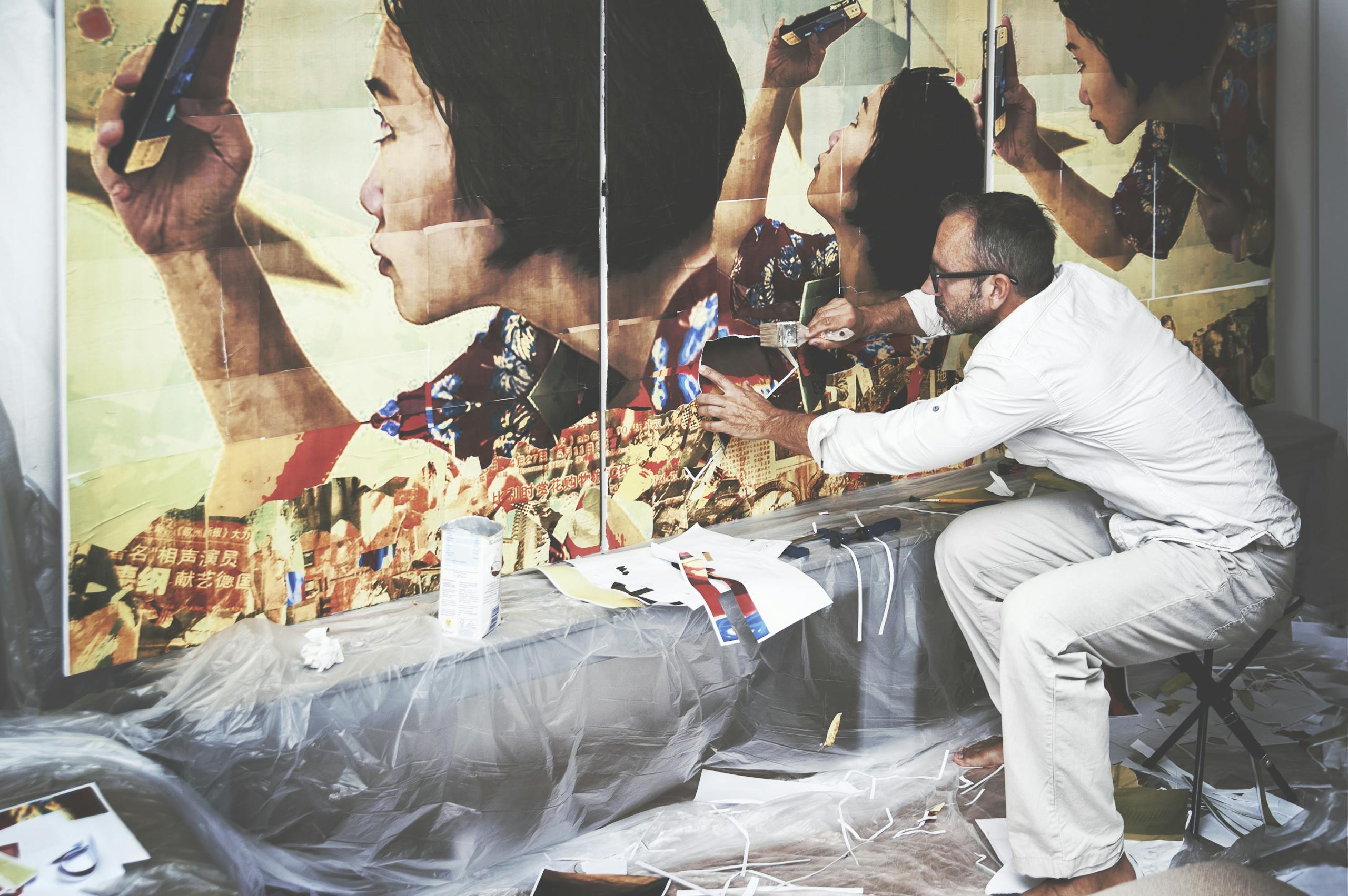 A man engaged in creating a large artistic collage indoors, capturing creativity and focus.